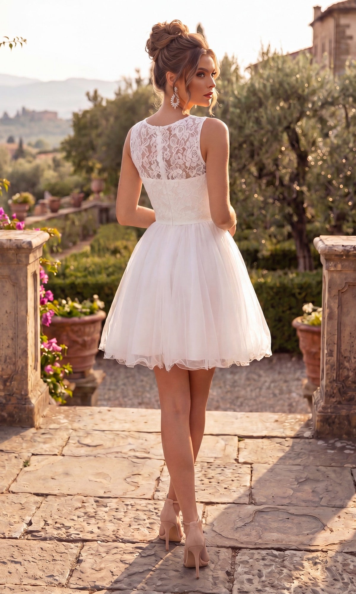 Wearing the Short Homecoming Dress: Chicas C1107, a woman in heels stands outdoors on a stone path, facing away, with greenery and distant buildings in the background.